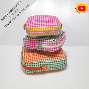 May include: Three square zippered pouches stacked vertically. The top pouch is pink and white gingham with a yellow trim. The middle pouch is green and white gingham with a white zip. The bottom pouch is orange and white gingham with green trim.