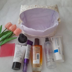 K&ouml;nnte beinhalten: Eine Kosmetiktasche aus Stoff mit Blumenmuster und hellviolettem Innenfutter, begleitet von drei k&uuml;nstlichen rosa Tulpen, einem rosa Kamm sowie sechs verschiedenen Hautpflegeflaschen und -tuben, darunter eine La Roche-Posay Cicaplast Baume B5+ Tube.