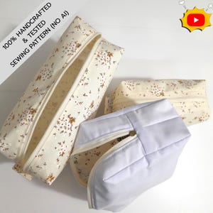 Puede incluir: Tres estuches con cremallera hechos de tela color crema con un pequeño estampado floral en marrón, rojo y verde. Los estuches varían en tamaño y forma, incluyendo uno rectangular largo, uno rectangular más pequeño y uno cuadrado.