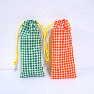 May include: Two small drawstring bags. One is green and white checkered, the other is orange and white checkered. Both have yellow drawstrings. The bags are upright against a white background.