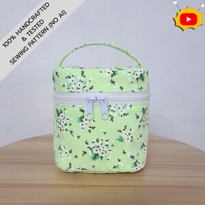 May include: A cylindrical fabric storage bag in light green with a white floral pattern. It features a top handle, a white zipper closure with two light purple pulls, and a text overlay stating 100% HANDCRAFTED & TESTED SEWING PATTERN (NO AI).