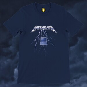 May include: A navy blue short-sleeve t-shirt featuring a graphic print of a vintage computer monitor centered beneath a lightning bolt design. The word METADATA is printed in a metallic, jagged font above the computer and lightning illustration.