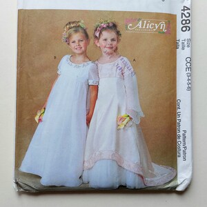 May include: A McCall's pattern for a girl's dress, size CCE (3-4-5-6). The pattern is for a white dress with a lace trim and a flower detail. The pattern is called Alicyn Exclusives.