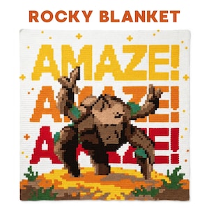 Può includere: Una coperta quadrata all'uncinetto con una creatura rocciosa marrone pixelata su un paesaggio giallo e marrone. Lo sfondo mostra il testo AMAZE! in lettere pixelate gialle, arancioni e rosse con piccoli segni più gialli sparsi ovunque.