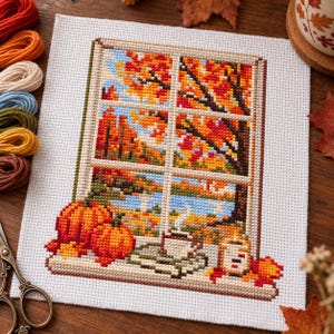 Peut inclure: Une broderie au point de croix sur tissu blanc représentant une vue par la fenêtre d'un paysage d'automne avec des arbres orange, un lac bleu et un ciel clair. Sur le rebord se trouvent deux citrouilles, une tasse fumante et une bougie.