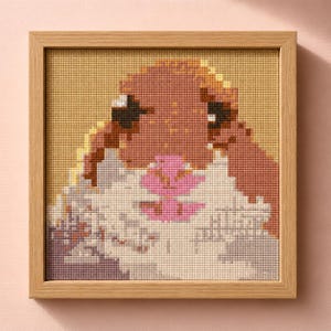 May include: A framed cross-stitch artwork featuring a pixelated bunny with brown fur, black eyes, and a pink flower. The bunny is set against a yellow background, and the frame is made of light-colored wood. The artwork is square.