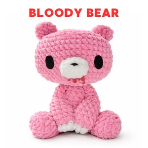 Puede incluir: Un oso rosa tejido a ganchillo con ojos negros, hocico blanco y detalles rojos que sugieren sangre. El texto "BLOODY BEAR" se muestra en rojo encima del oso. El oso está sentado con los brazos y las piernas al frente.