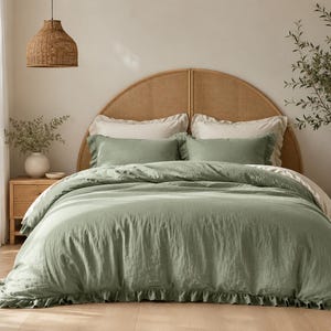 Peut inclure: Une housse de couette vert sauge avec un bord à volants, accompagnée de deux taies d'oreiller assorties à volants et de deux oreillers blanc cassé unis. La literie est placée contre une tête de lit arrondie en cannage marron clair.