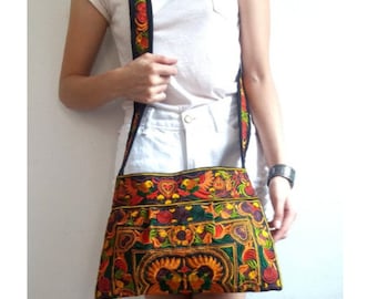 May include: A black and multi-colored embroidered shoulder bag with floral and geometric patterns. The bag has a long strap and is worn over the shoulder.