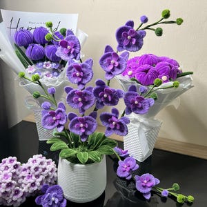 May include: Handmade purple orchid arrangements, including potted plants, bouquets, and individual flowers. The orchids feature detailed petals and are displayed in white pots and wrapped bouquets. The text "Happy" is visible.