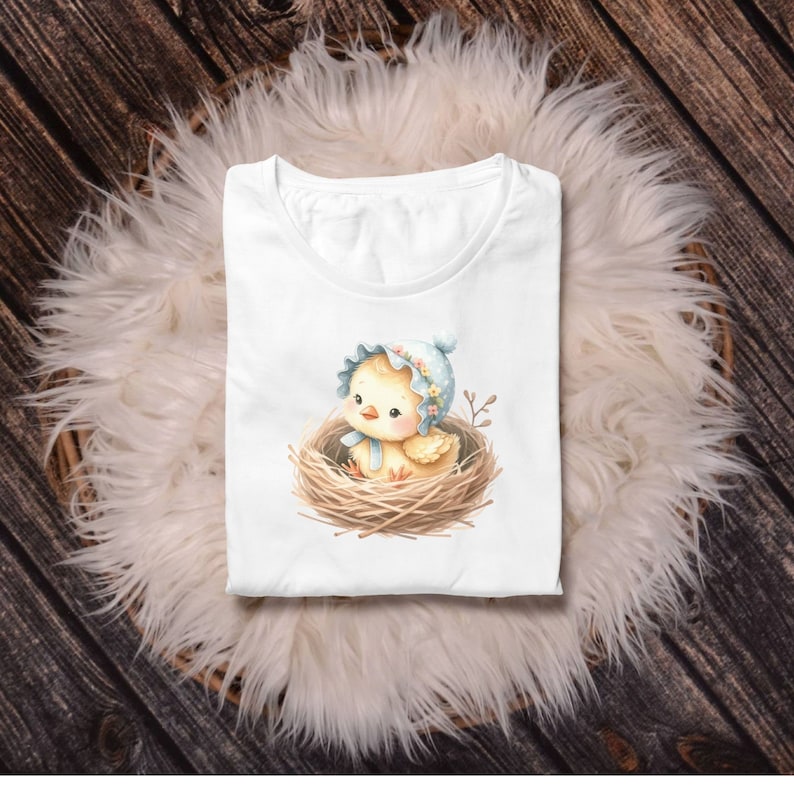May include: White t-shirt with a cute cartoon chick wearing a blue bonnet and sitting in a nest.