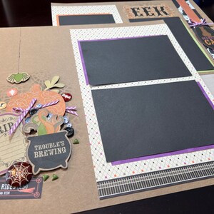 May include: A scrapbook page with a brown background and black and white patterned paper. The page features a cauldron with the text "Trouble's Brewing", a spider web, a tombstone with the text "RIP", and a pumpkin. The page also includes a black and white patterned paper with the text "EEK" and a black and white patterned paper with the text "Spooky Cat".