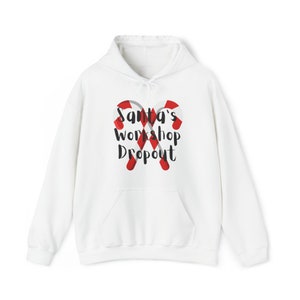 May include: White hooded sweatshirt with a graphic of two candy canes crossed over each other. The text "Santa's Workshop Dropout" is printed in black on the front of the sweatshirt.