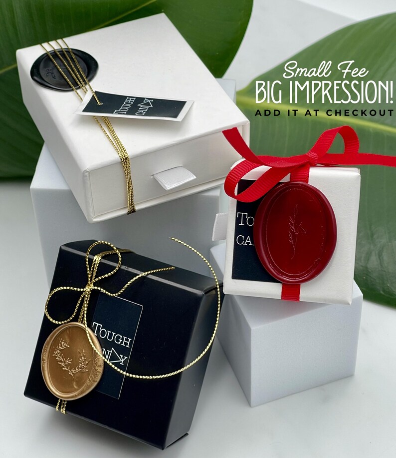 three gift boxes with various designs and colors, including a white box with a red ribbon, a black box with a gold ribbon, and a white box with a red ribbon. The boxes are placed on a white surface, and there is a green leaf in the background.