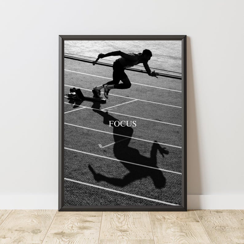 May include: Black and white framed print of a sprinter in motion on a track. The word "FOCUS" is printed in white below the runner. The runner's shadow is cast on the track.