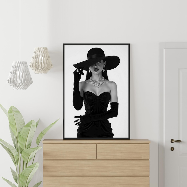 May include: Black and white framed print of a woman in a black dress, hat, and gloves. The woman is wearing a diamond necklace and earrings. The image is displayed on a wooden dresser.