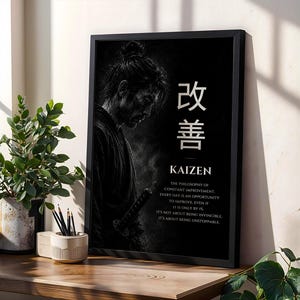 Op de afbeelding: Een zwart ingelijste kunstprint met een monochrome illustratie van een samoerai in profiel. De tekst bevat de Japanse kanji voor Kaizen, het woord Kaizen en een alinea die de filosofie van constante verbetering uitlegt.