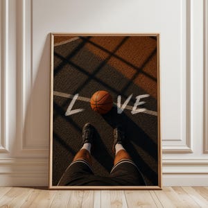 May include: A framed wall art print featuring a first-person perspective of a basketball court with a basketball resting on the ground. The word LOVE is written in white brushstroke lettering across the court surface, with dark shadows cast.