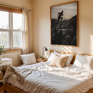 May include: A large rectangular wall art print featuring a black and white silhouette of a person running up a rocky mountain slope against a bright sky, with the word DISCIPLINE printed in white capital letters centered below the runner.