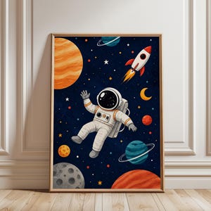 Könnte beinhalten: Ein gerahmter Wandkunstdruck mit einem Cartoon-Astronauten, der im Weltraum schwebt. Der dunkelblaue Hintergrund ist mit Sternen, einem großen orangefarbenen Planeten, einem roten Planeten, einem Kratermond und einer Rakete gefüllt.