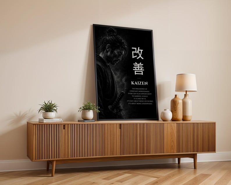 Op de afbeelding: Een zwart ingelijste verticale wandprint met een monochroom portret van een samoerai met een zwaard, de Japanse kanji voor Kaizen en Engelse tekst die de filosofie van constante verbetering uitlegt op een donkere achtergrond.