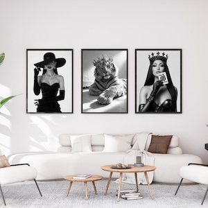 May include: Three framed black and white art prints. The prints feature a woman in a hat and gloves, a tiger wearing a crown, and a woman in a crown holding a playing card. The art is displayed above a white sofa.