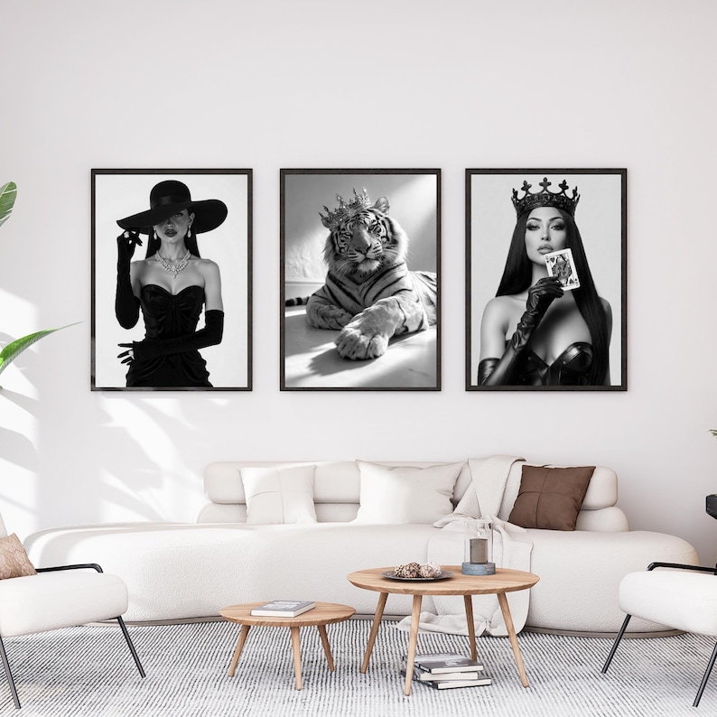 May include: Three framed black and white art prints. The prints feature a woman in a hat and gloves, a tiger wearing a crown, and a woman in a crown holding a playing card. The art is displayed above a white sofa.