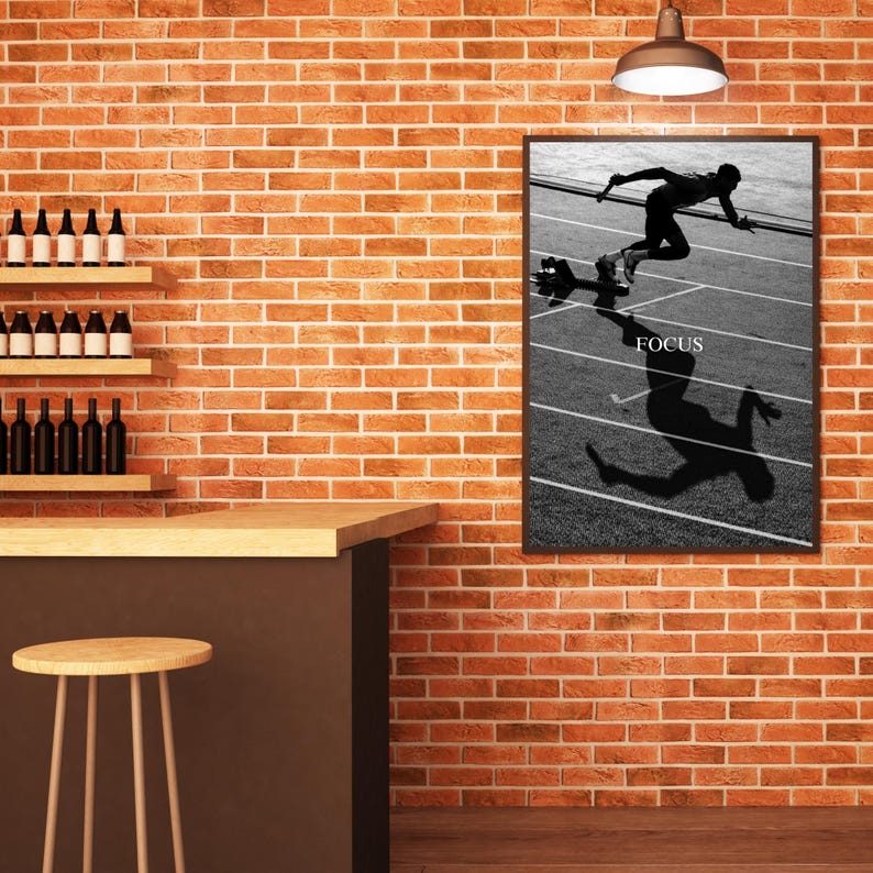 May include: Black and white framed print of a runner on a track, with the word "FOCUS" in white. The runner is in mid-stride, with a long shadow cast on the track. The print is hanging on a brick wall.