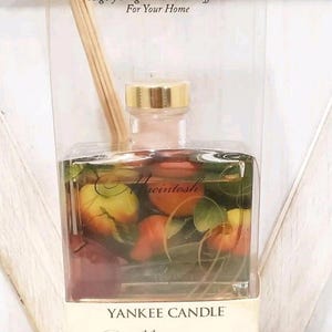 May include: Yankee Candle Macintosh reed diffuser. The glass bottle contains a liquid with apple and leaf imagery. The product is in a clear plastic box with the brand name and product name printed on the label. The bottle contains 3 fl oz (88.7ml).