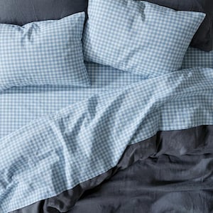 Könnte beinhalten: Draufsicht auf ein Bett mit hellblau-weiß karierter Bettwäsche. Das Set beinhaltet zwei Kissenbezüge und ein Spannbettlaken. Das untere Laken ist einfarbig dunkelgrau.