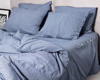 Puede incluir: Un juego de cama a rayas azules y blancas con una almohada blanca y una lámpara de pie negra en un dormitorio con una pared de hormigón.