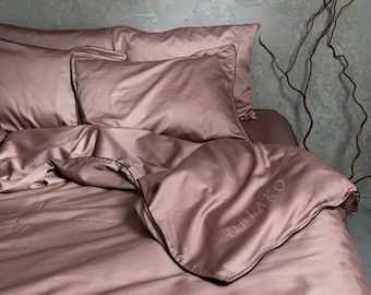 May include: A dusty rose colored bedding set with black trim. The duvet cover has the word "OBLAKO" embroidered on it.