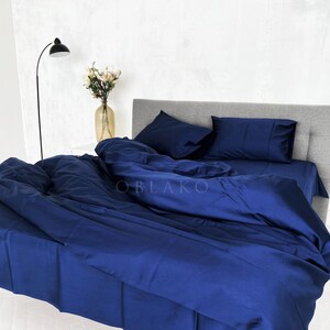 Op de afbeelding: Een donkerblauwe dekbedovertrekset met twee bijpassende kussenslopen. De beddengoed is gemaakt van een zachte, gladde stof en is kreukvrij. De set wordt getoond op een bed met een grijs hoofdeinde.
