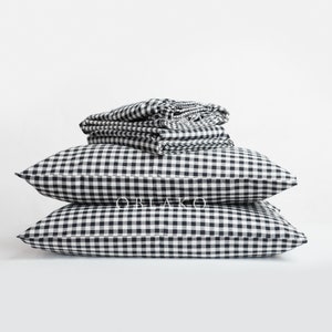 Puede incluir: Una pila de fundas de almohada a cuadros negros y blancos y dos fundas de almohada a juego. Las fundas de almohada están dobladas y apiladas sobre un fondo blanco.
