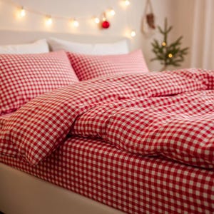 May include: A bed with red and white gingham bedding. The set includes a fitted sheet, a duvet cover, and two pillowcases. The room is decorated with string lights and a small Christmas tree.