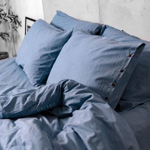 May include: A blue duvet cover and pillowcases with a subtle texture. The duvet cover has the word "OBLAKO" printed on it.
