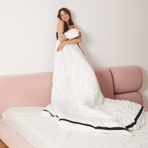 Pode incluir: Uma capa de edredom branca com uma borda preta, deitada em uma cama rosa. Uma pessoa est&aacute; em p&eacute; na cama, segurando a capa de edredom.
