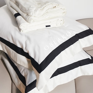 Pode incluir: Roupa de cama branca com acabamento preto e a palavra "OBLAKO" bordada na fronha.
