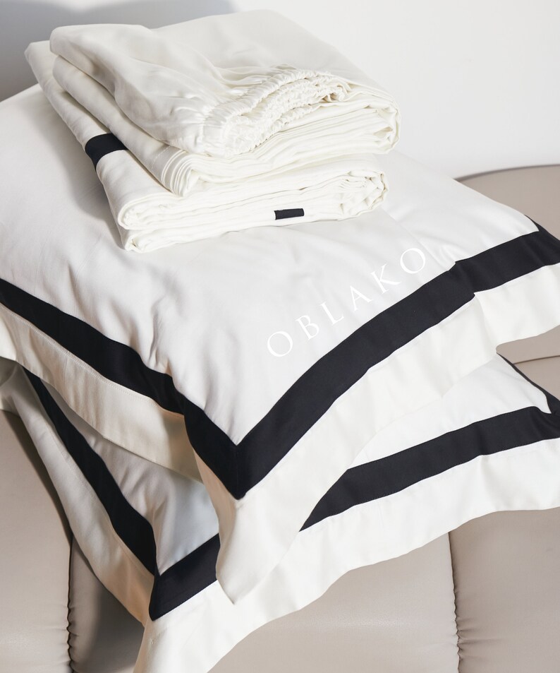 Pode incluir: Roupa de cama branca com acabamento preto e a palavra "OBLAKO" bordada na fronha.