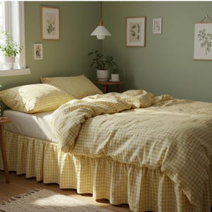 May include: A bed with yellow and white gingham bedding, including a comforter, pillow, and bed skirt. The room has a light green wall, framed botanical prints, and a small rug. The word "OBLAKO" is visible on the bedding.