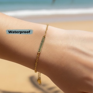 May include: A gold-colored bracelet with a delicate chain and a rectangular bar pendant. The pendant is engraved with the text "Jeremiah 29:11". The word "Waterproof" is displayed in a blue rectangle. The bracelet is shown on a wrist.
