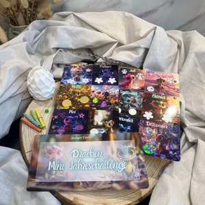 Op de afbeelding: Een kleurrijke maandelijkse kalender met een drakenthema. Elke maand heeft een andere drakenillustratie en een lege cirkel om de voortgang bij te houden. De kalender heeft de titel "Budget Turtle Drachen Mini Jahreschallenge".