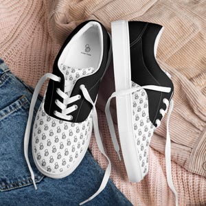 May include: Pair of black and white canvas sneakers. The sneakers feature a black heel and tongue, white laces, and a white sole. The canvas is patterned with a repeating black and white design. The interior of the shoe is white with a small logo.