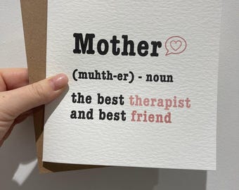 May include: A white greeting card with the word "Mother" in bold black font, followed by a definition. The card includes the phrases "the best therapist and best friend" in pink and black. A brown envelope is behind the card.