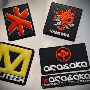 Könnte beinhalten: Eine Sammlung schwarzer rechteckiger Aufnäher mit verschiedenen Designs. Einer zeigt einen roten Stern, ein anderer eine flammende orangefarbene Samurai-Maske mit dem Wort "SAMURAI". Weitere Aufnäher zeigen die Texte "MILITECH" und "ARASAKA".