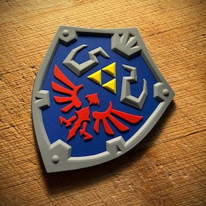 May include: A blue, gray, and red shield with a stylized design. The shield features a blue center with red and yellow accents, and a gray border. The shield is likely a decorative item or a collectible.