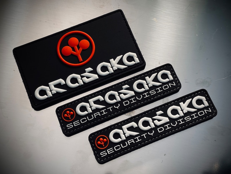 May include: Black rectangular patches with the word "ARASAKA" in white, stylized lettering. One patch has an orange logo. Two smaller patches read "ARASAKA SECURITY DIVISION".