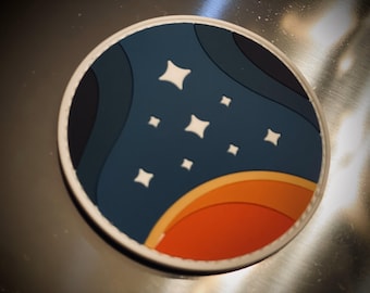 Puede incluir: Un parche redondo blanco con un diseño azul y naranja. La sección azul presenta un patrón ondulado y estrellas blancas. La sección naranja es una forma de media luna.