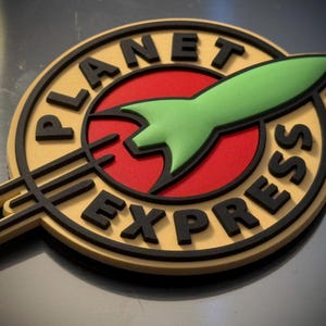 Puede incluir: Logotipo circular de Planet Express con un cohete verde, un círculo rojo y letras negras. El logotipo tiene un esquema de color dorado y negro, con las palabras "PLANET EXPRESS" en un lugar destacado.