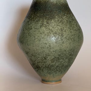 Può includere: Un vaso in ceramica fatto a mano con una forma a diamante unica. Il vaso presenta una smaltatura verde macchiata che si scurisce verso l'alto. Il bordo e la base hanno un aspetto naturale non smaltato, aggiungendo un tocco rustico. Un oggetto decorativo per la casa.